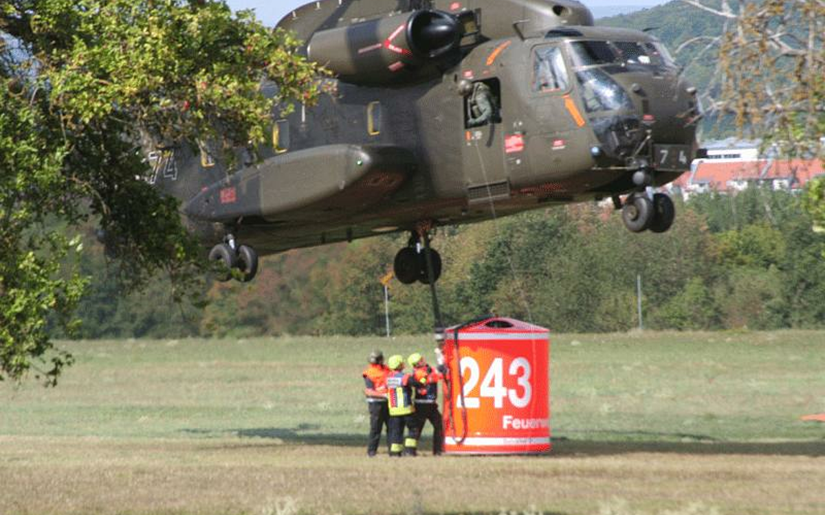 Ein Hubschrauber mit Löschtank schwebt knapp über dem Boden Ein Hubschrauber mit Löschtank schwebt knapp über dem Boden